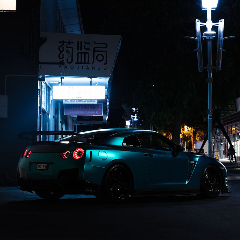 Teal car at night infront of shops