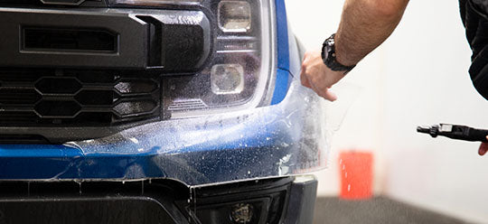 A person applying PPF to the front bumper of a Ford Raptor