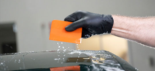 A person wearing a black glove holding an orange PPF squeege