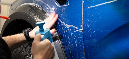 A person spraying PPF application solution on a blue car