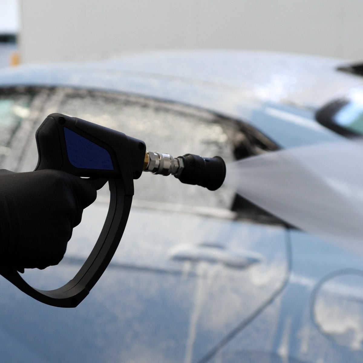 A person washing a blue car with a MTM short gun and nozzle