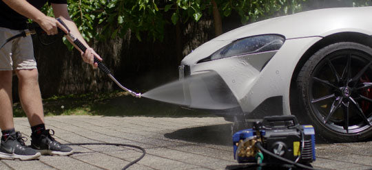 Person using an Annovi Reverberi pressure washer to clean a white sports car outdoors.